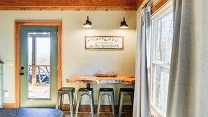 A room with a wooden ceiling, a door leading outside, a table with stools, and a sign on the wall.
