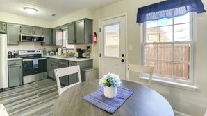 A modern kitchen with stainless steel appliances, a dining table with chairs, and a window with a blue valance.
