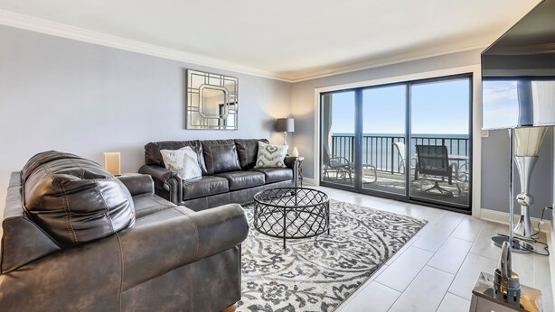A modern living room with a leather sofa, a patterned rug, and a large window with a view of the outdoors.