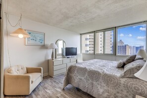 Une chambre à coucher comprenant un lit, une chaise, un téléviseur et une fenêtre donnant sur la ville.