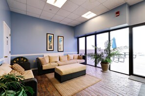 Un hall d’hôtel avec un mur bleu, deux œuvres d’art encadrées, un canapé, une grande fenêtre et une plante en pot.