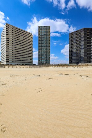 Trois immeubles de grande hauteur se dressent sur une plage de sable fin, sous un ciel dégagé.