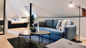 Een moderne loft slaapkamer met een schuine plafond, een blauwe bank, een ronde salontafel en een vloerlamp.