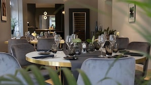 Een eetgedeelte met ronde tafels, grijs gestoffeerde stoelen en een modern interieur.