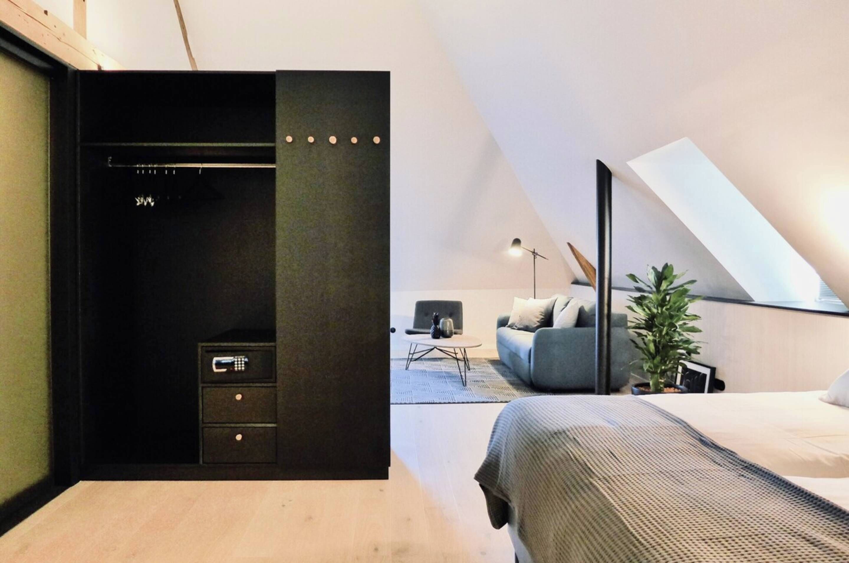 A modern bedroom with a loft-style ceiling, a bed, a sofa, a desk, and a wardrobe.