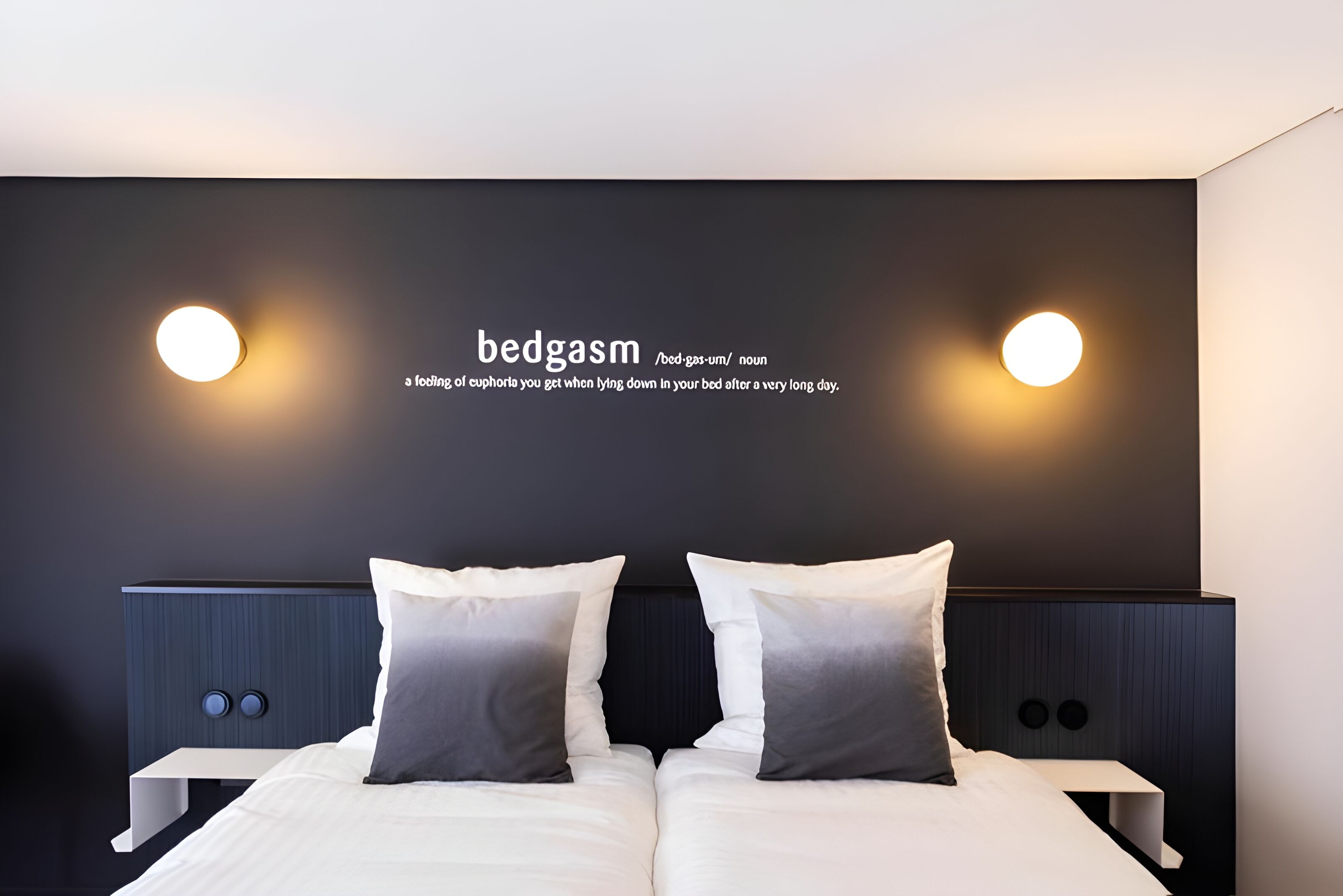 Een moderne slaapkamer met een groot bed, twee nachtkastjes en een donkere wand met twee ronde wandlampen.