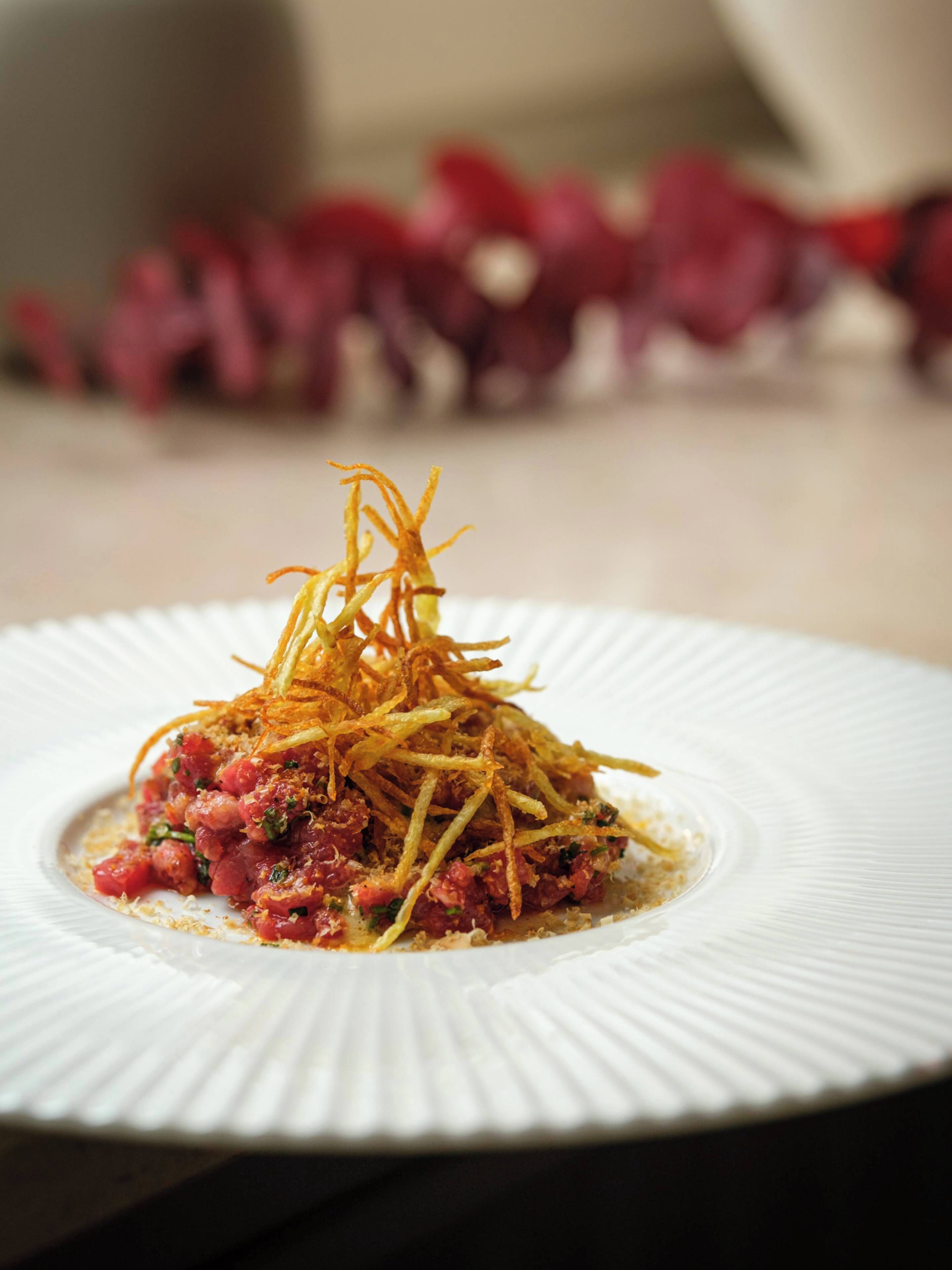 Une assiette blanche contenant un plat, peut-être un tartare, garni de fines lanières croustillantes.