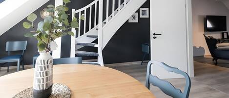 Un salon moderne avec un escalier, une table à manger agrémentée d’un vase et des chaises bleues.
