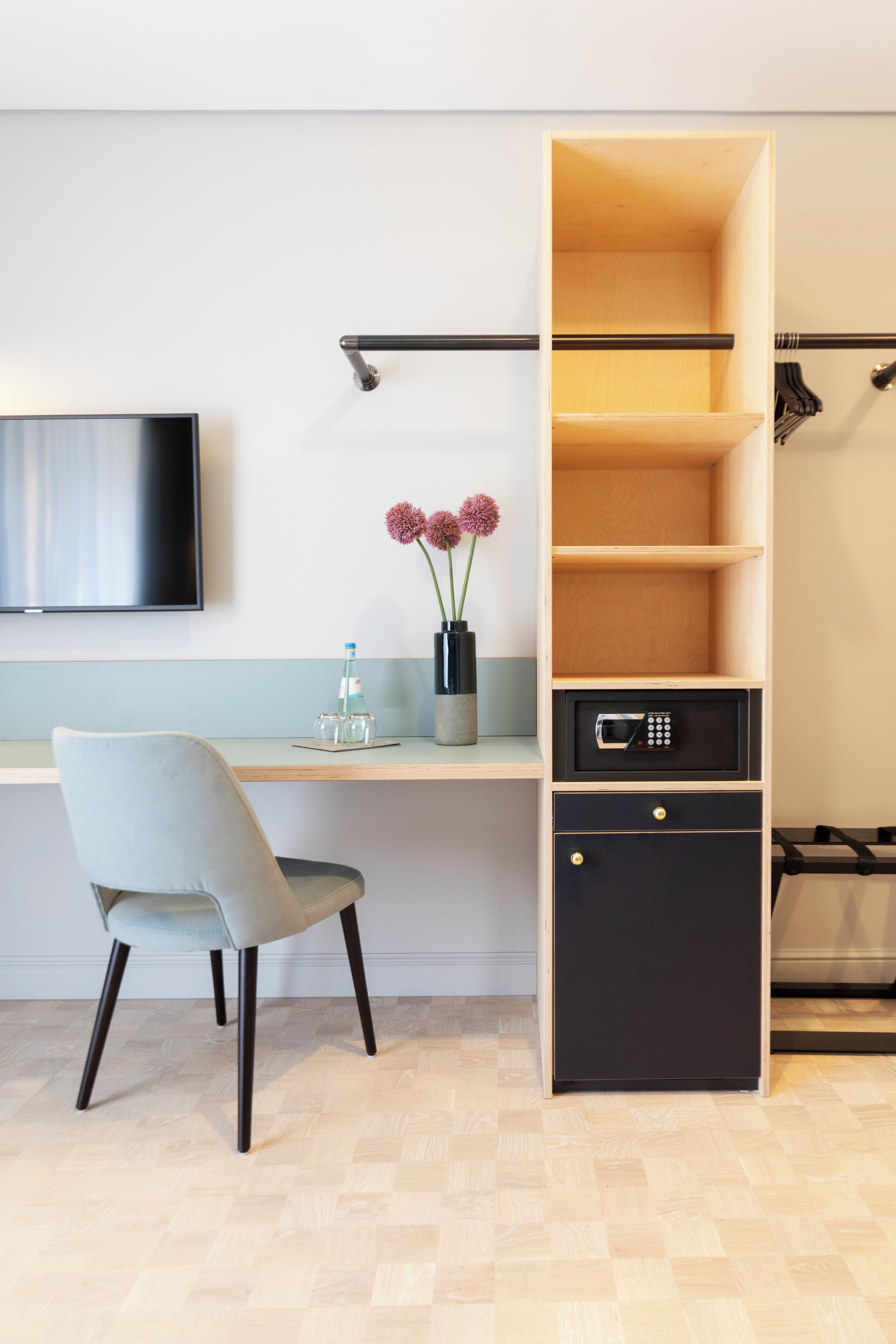 A modern room with a wooden desk, a chair, a flat-screen TV, a small vase with flowers, and a microwave in a cabinet.