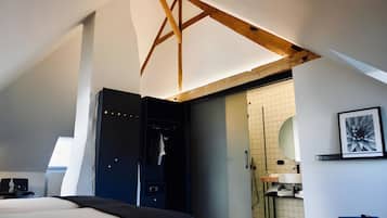 A modern hotel room with a sloped ceiling, a walk-in closet, a bathroom with a tiled wall, and a framed picture on the wall.
