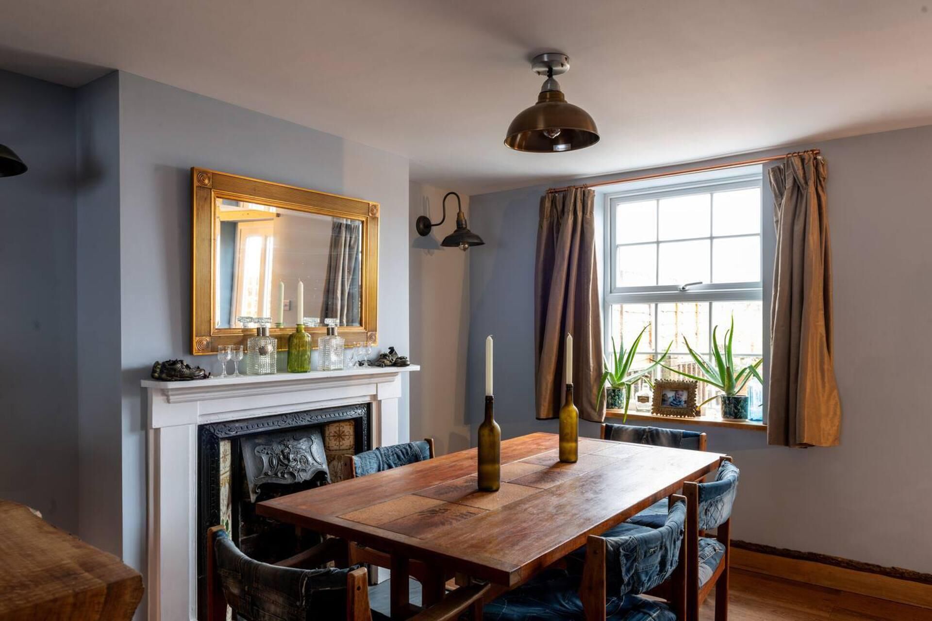 A dining area with a wooden table and chairs, a fireplace, a large mirror, and a window with curtains.