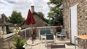 A patio area with a table and chairs, a potted plant, and a red umbrella.