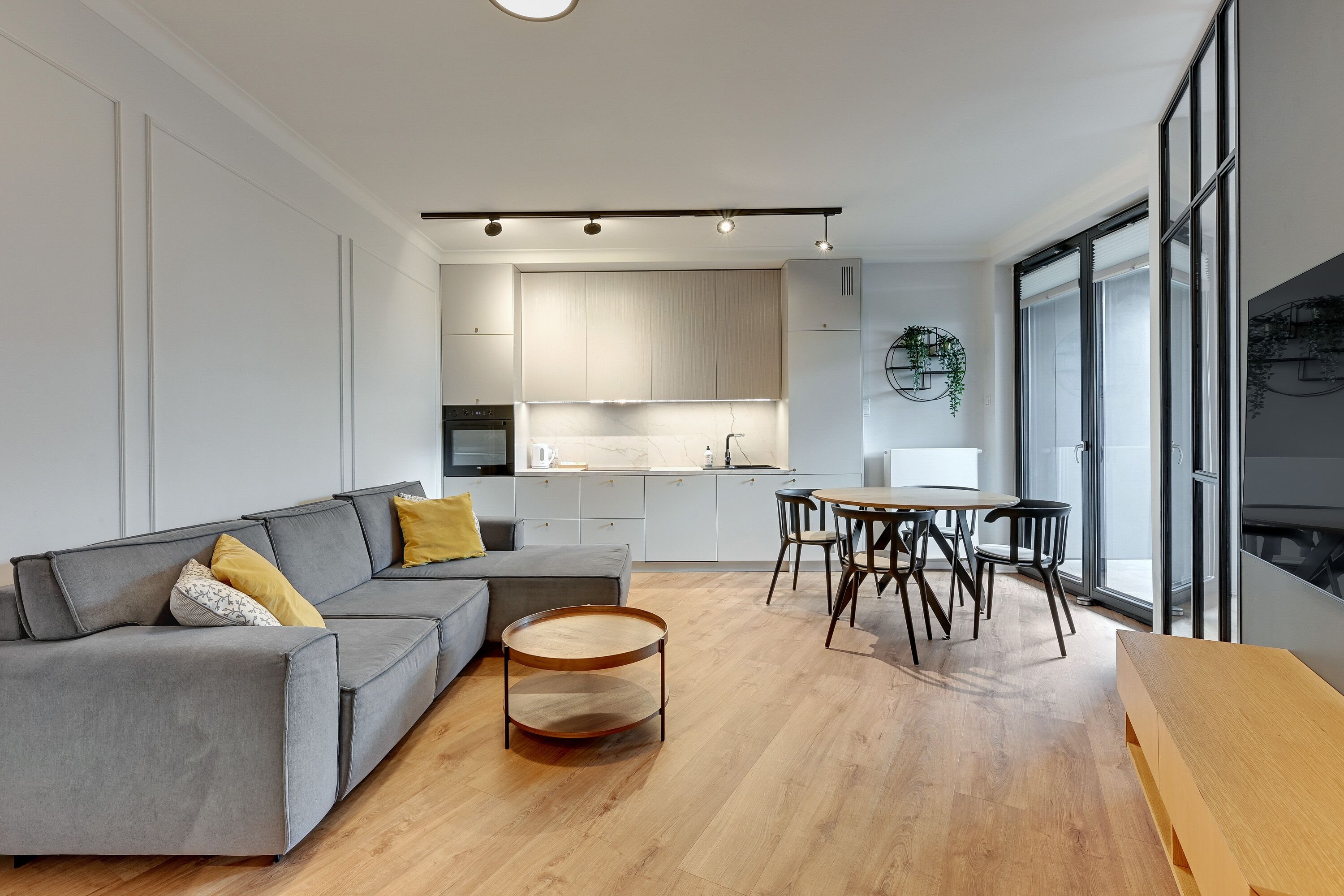 Un salon moderne avec un canapé gris, une table basse en bois et un coin repas comprenant une table ronde et des chaises.