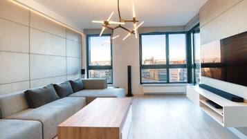 Una sala de estar moderna con un sofá modular, una mesa de centro de madera, un televisor grande y ventanas amplias con vistas a la ciudad.