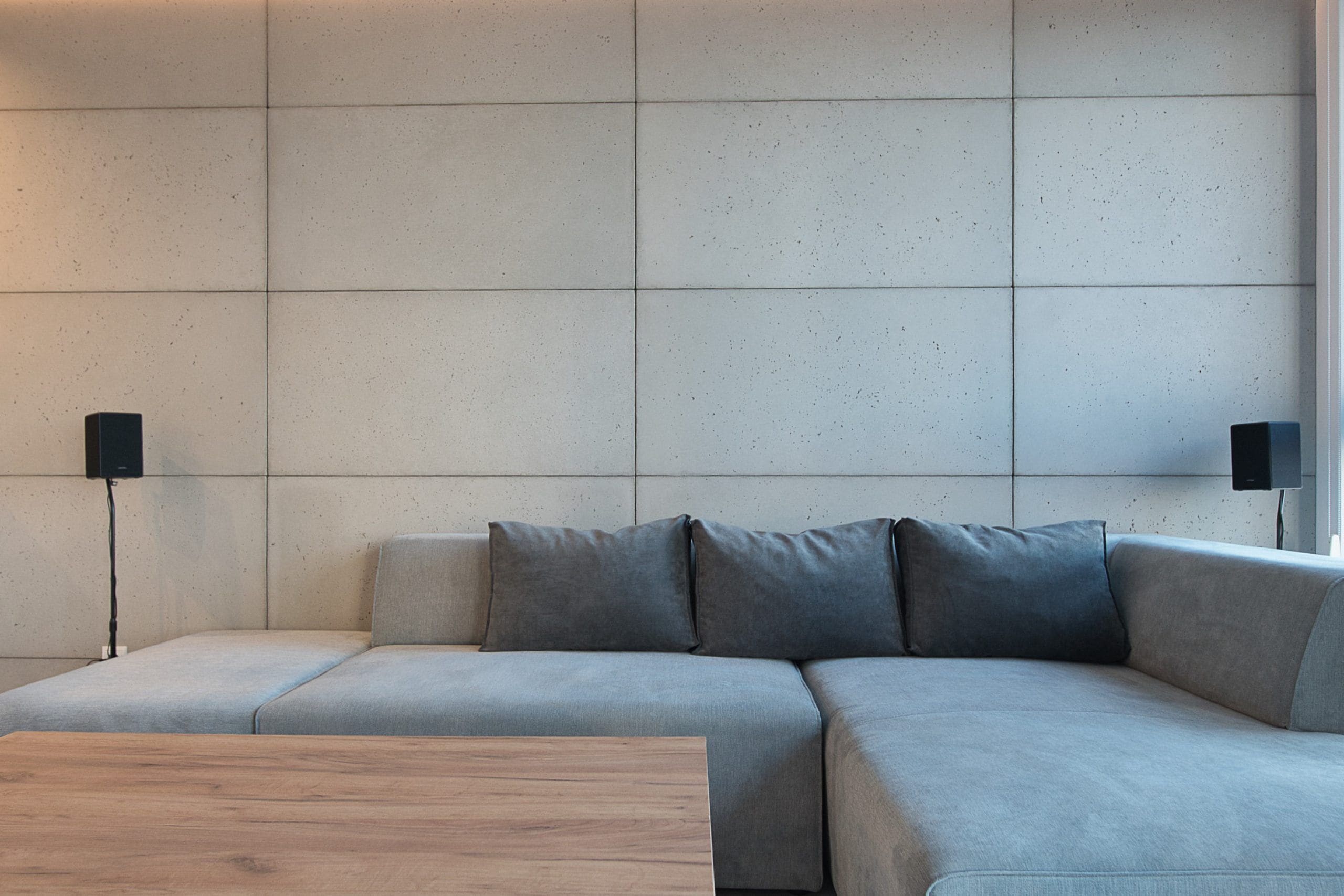 Un salon moderne avec un canapé d’angle gris, une table basse en bois et deux lampadaires noirs.