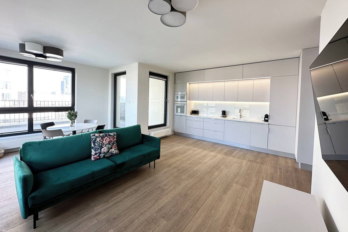 A modern apartment with a green sofa, a dining area, and a kitchen with integrated appliances.