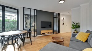 Uma sala de estar moderna com um sofá cinzento, uma mesa de jantar de madeira e uma TV fixada na parede.