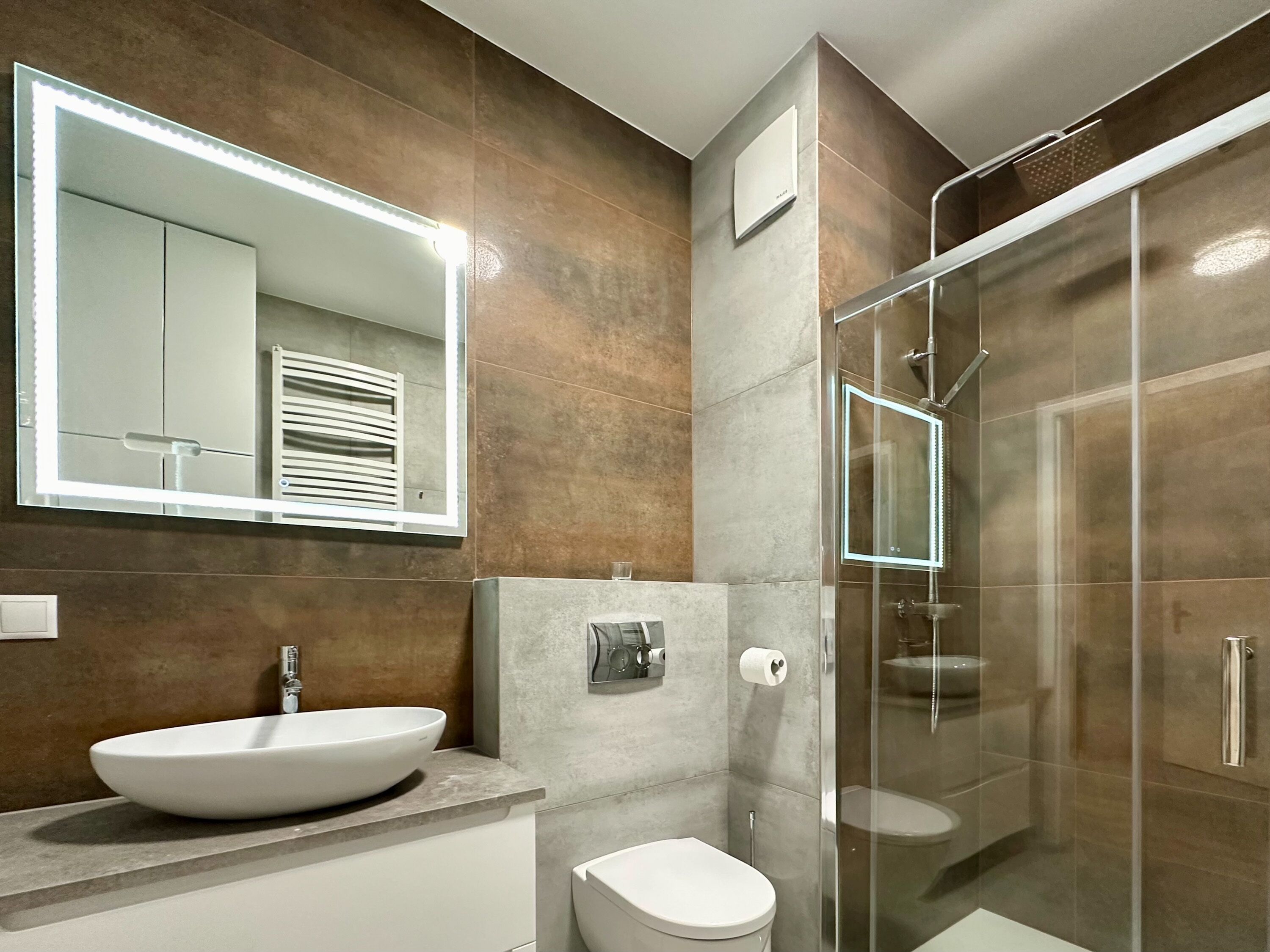 A modern bathroom with a large mirror, a vessel sink, a toilet, and a glass-enclosed shower.