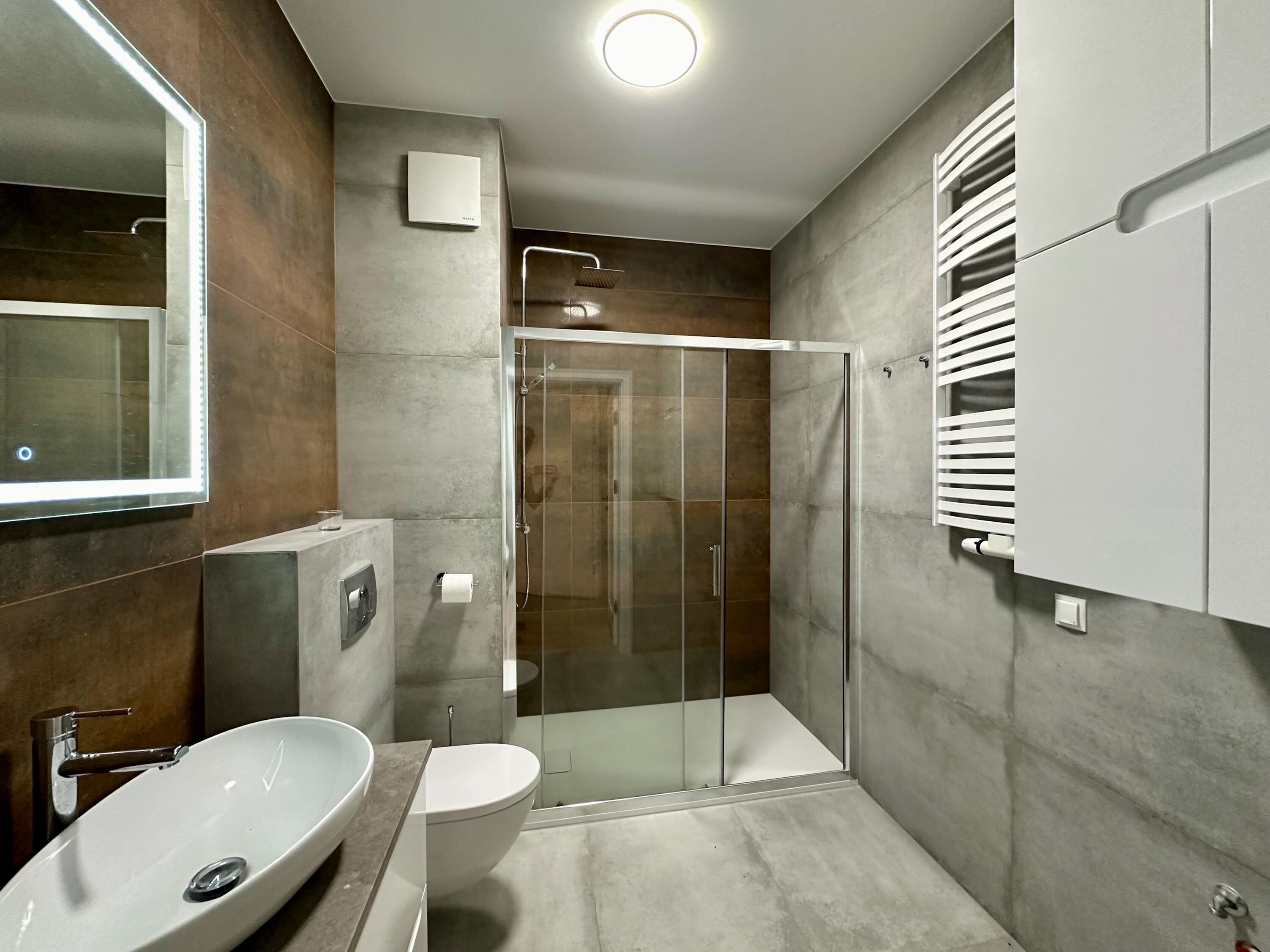 Un bany modern amb plat de dutxa envoltat de vidre, un mirall gran i un lavabo blanc.