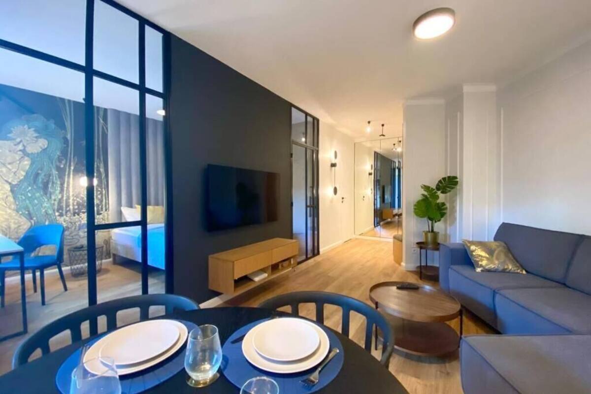A modern living room with a sofa, a coffee table, and a dining area with chairs and a table set for two.