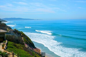 A coastal view with a building adjacent to the ocean, featuring a balcony with railings and a staircase leading down to the beach. - Beachfront Bliss - Panoramic Ocean Views in Solana Beach (Solana Beach)