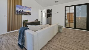 A modern living room with a white sofa, a cityscape painting, and a wooden accent wall. - Disney Villa w Priv Pool & Lake View-12 Mi parks Top 1% Listing on A i r b n b (Kissimmee)