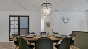 A dining area with a large wooden table set for six, surrounded by black chairs with wooden legs. A chandelier hangs from the ceiling, and there are two wall-mounted mirrors above the table. - Disney Villa w Priv Pool & Lake View-12 Mi parks Top 1% Listing on A i r b n b (Kissimmee)