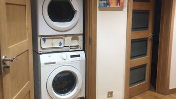 A laundry area with stacked washing machines and dryers, wooden doors, and a wall-mounted poster.
