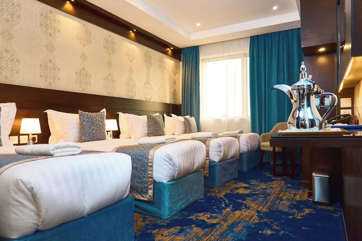 A hotel room with three beds, a desk, a coffee maker, and a view of the city.
