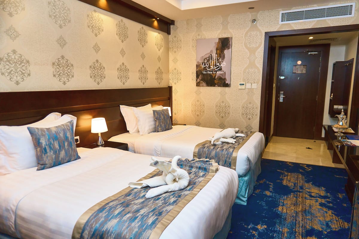 A hotel room with two beds, a blue carpet, and a wall with a decorative pattern.