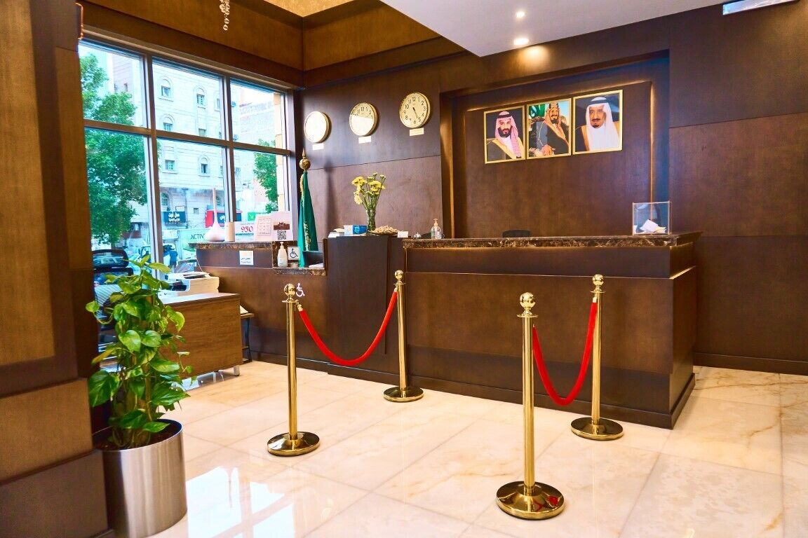 A reception area with a reception desk, red velvet ropes, clocks, and framed pictures on the wall.