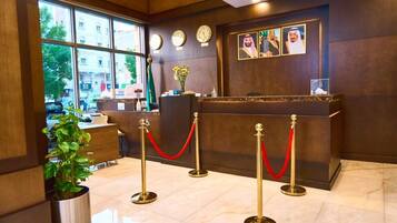 A reception area with a reception desk, red velvet ropes, clocks, and framed pictures on the wall.