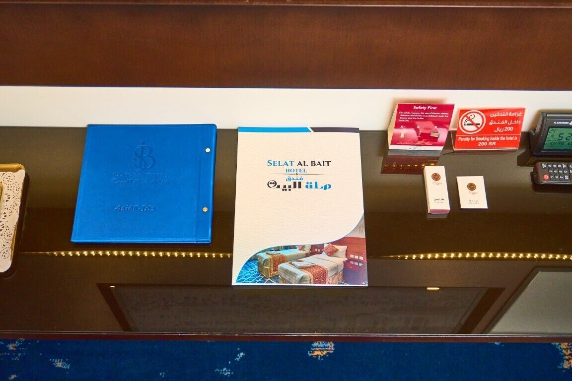 A reception desk with a blue folder, a welcome brochure, a safety fire sign, a no-smoking sign, and a digital clock.