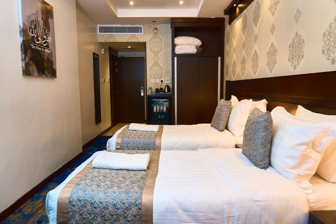 Quarto de hotel com duas camas, um minibar e uma parede com um padrão decorativo.