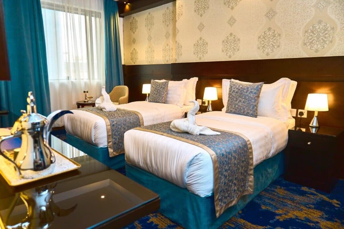 A hotel room with two beds, a desk with a lamp, and a view of the outdoors.