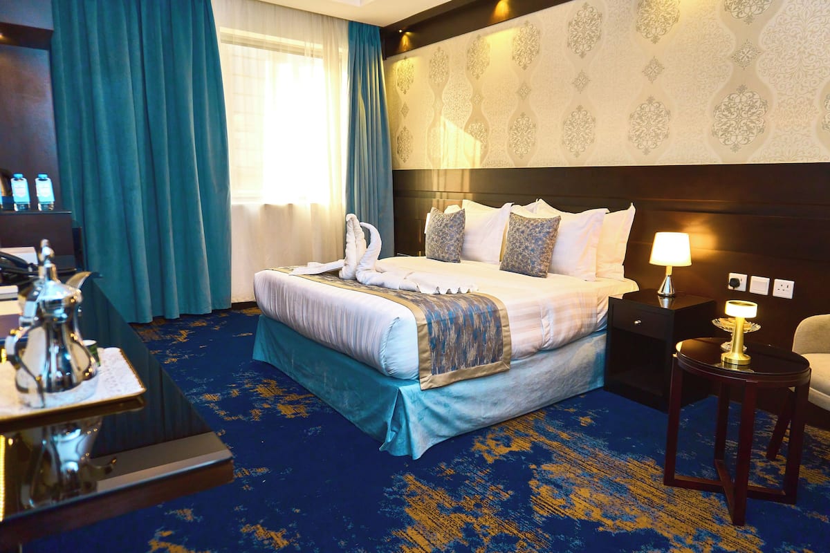 A hotel room with a large bed, a nightstand, a chair, and a desk with a lamp.