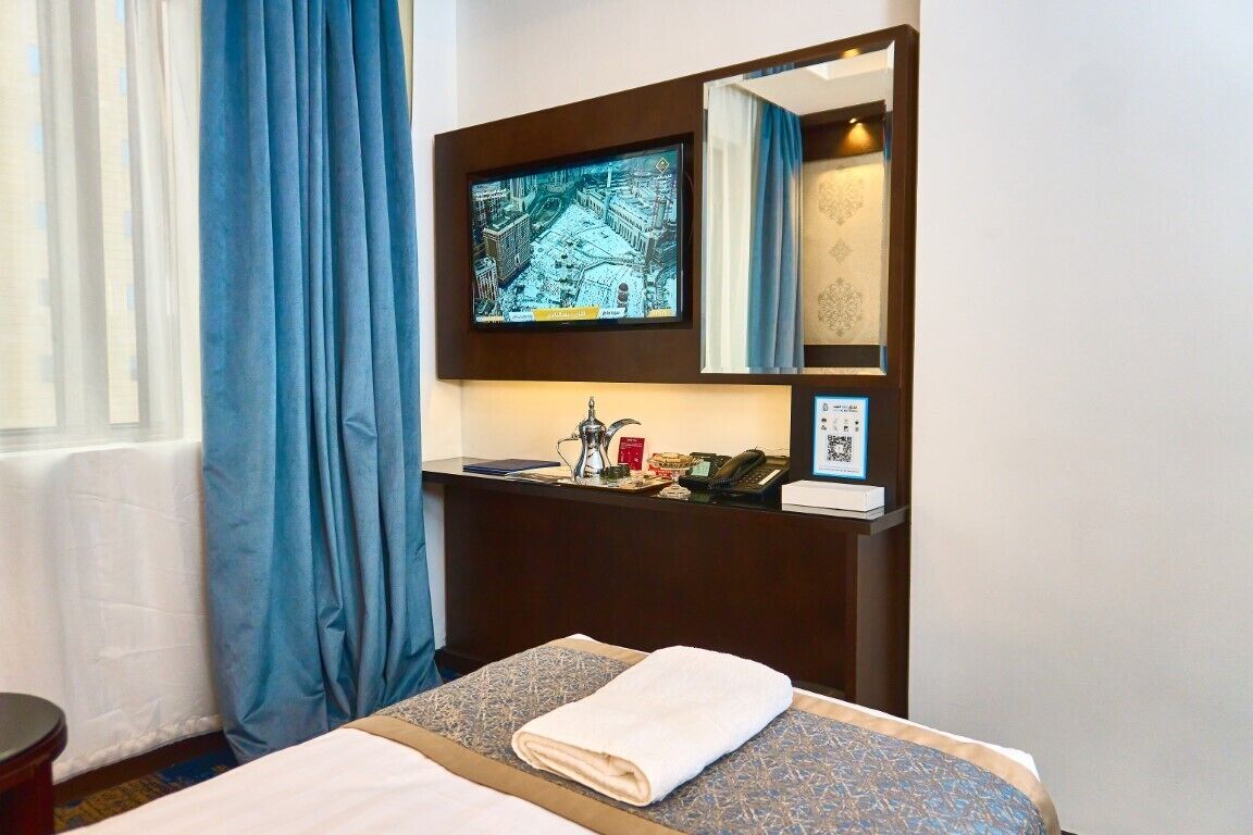 A hotel room with a bed, a desk with a telephone and a television, and a window with blue curtains.