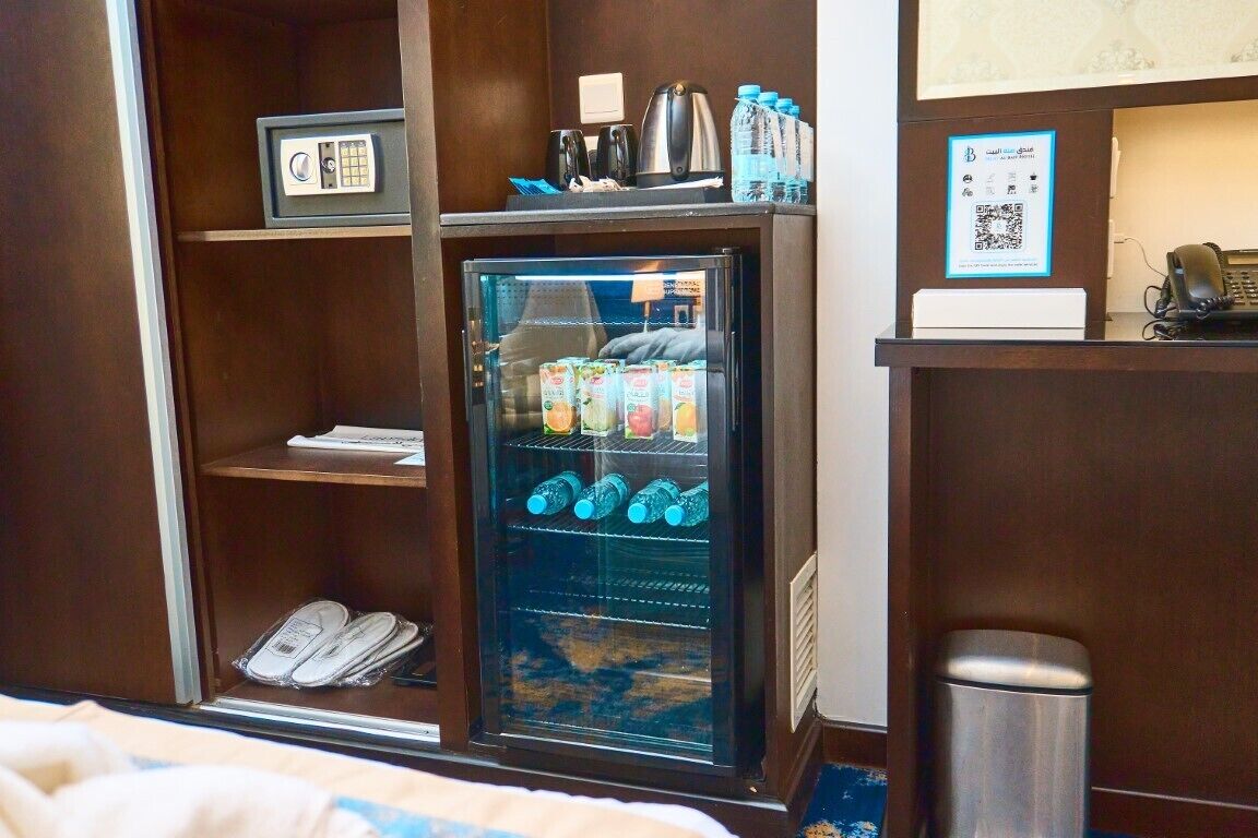 A hotel room with a minibar, a refrigerator stocked with beverages, a kettle, and a kettle holder.