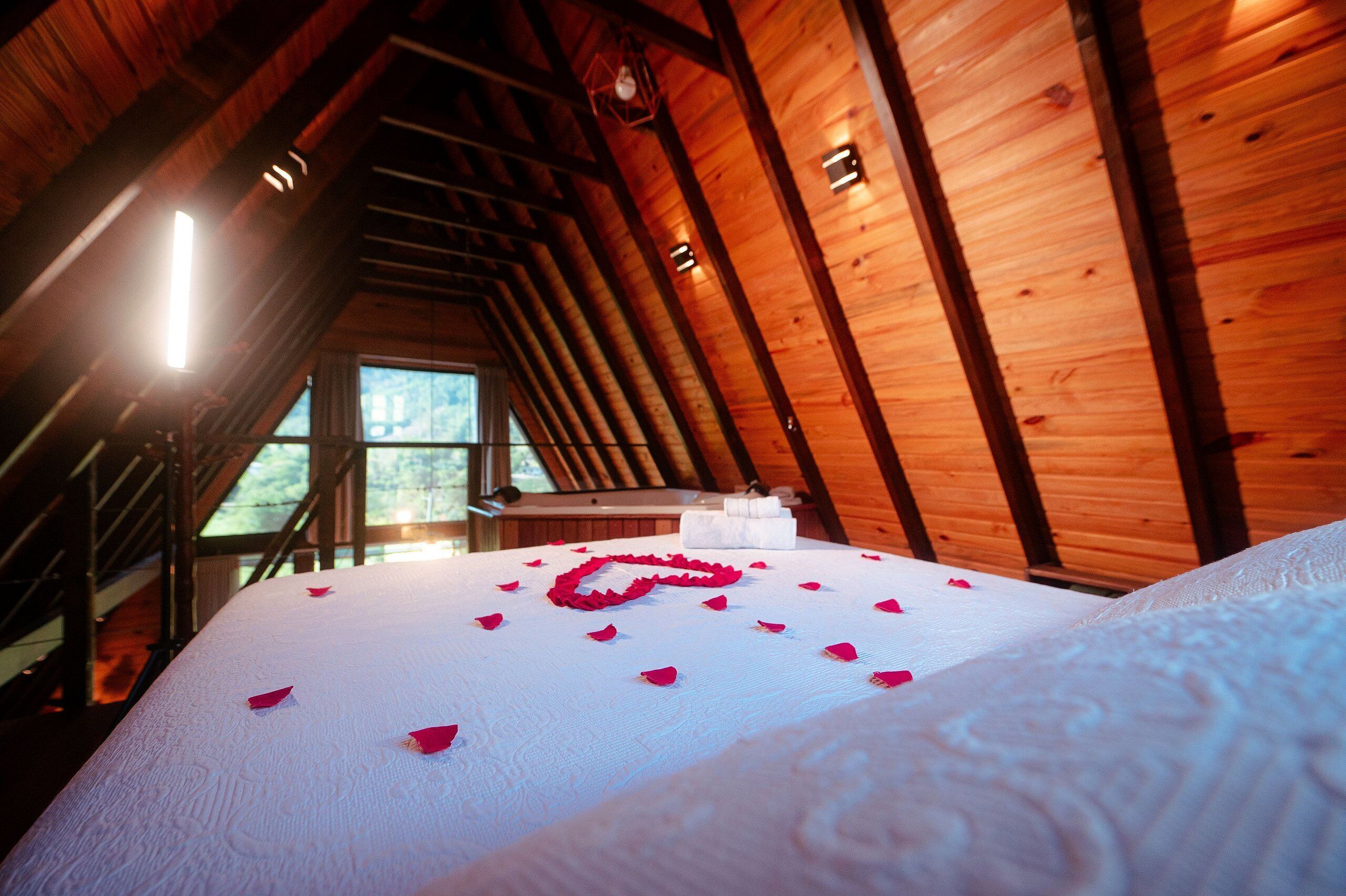 Ein Zimmer mit hohen Decken und Holzbalken, ein Bett mit weißer Bettwäsche und einer herzförmigen Dekoration.
