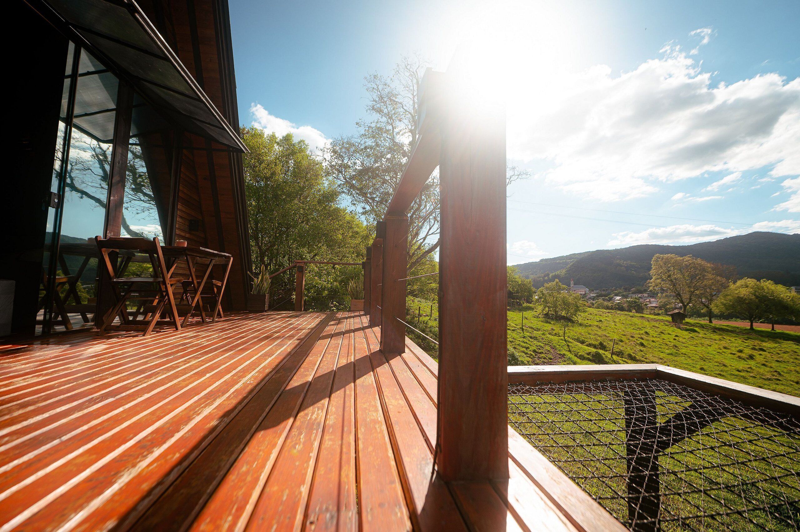 A wooden deck with chairs, a glass door, and a view of a green landscape.