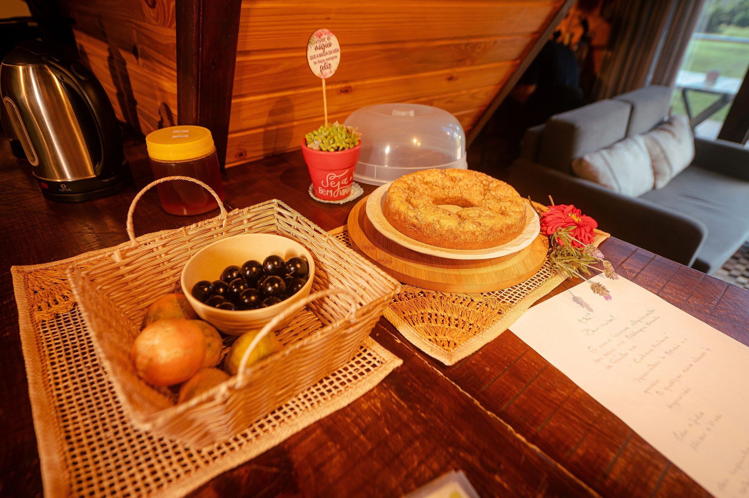 Een houten tafel met een mand vol fruit, een schaal olijven, een pot honing, een taart en een menukaart.