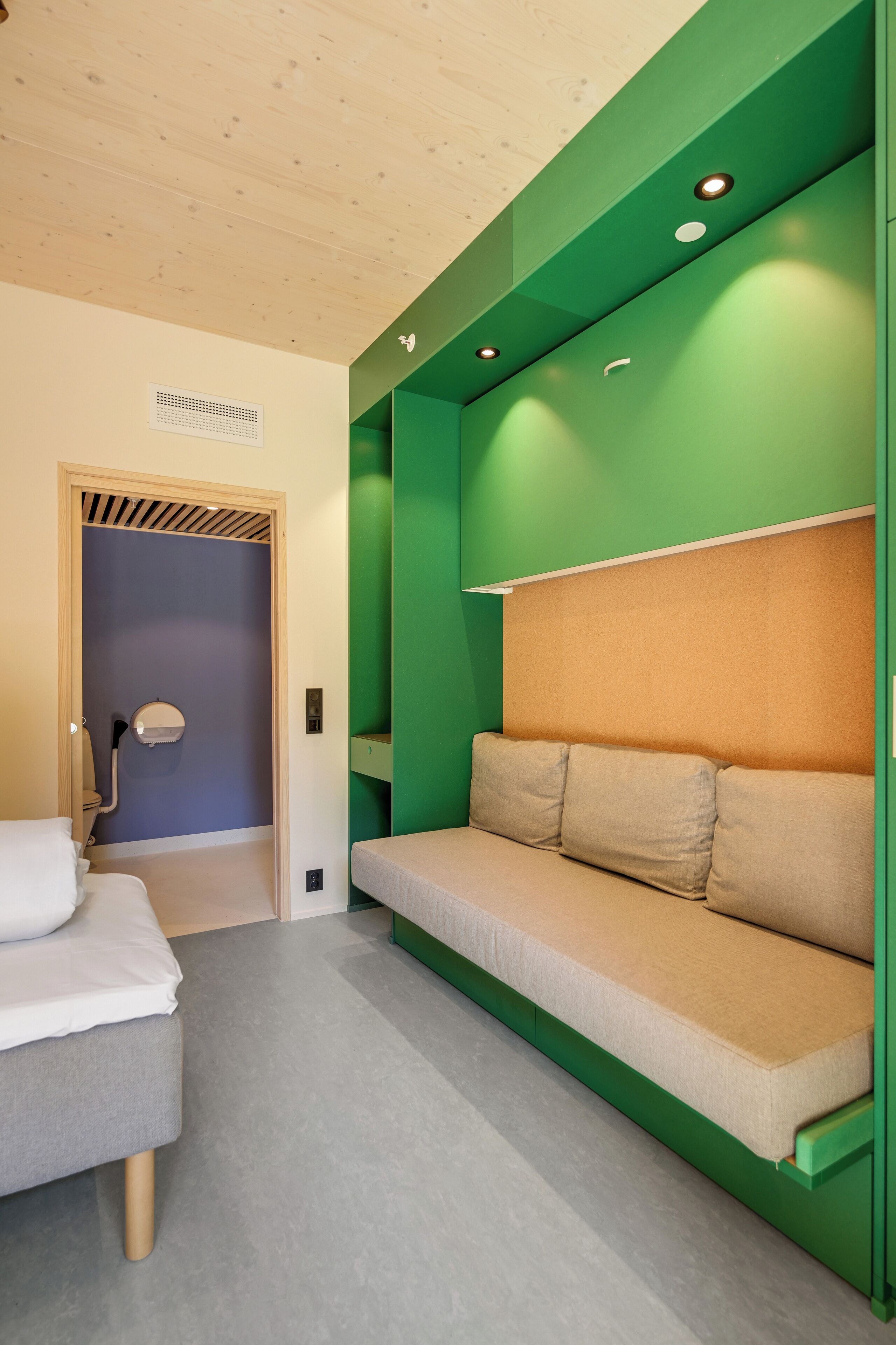 Una habitación con cama, sofá verde, techo de madera y una puerta que da a un baño.