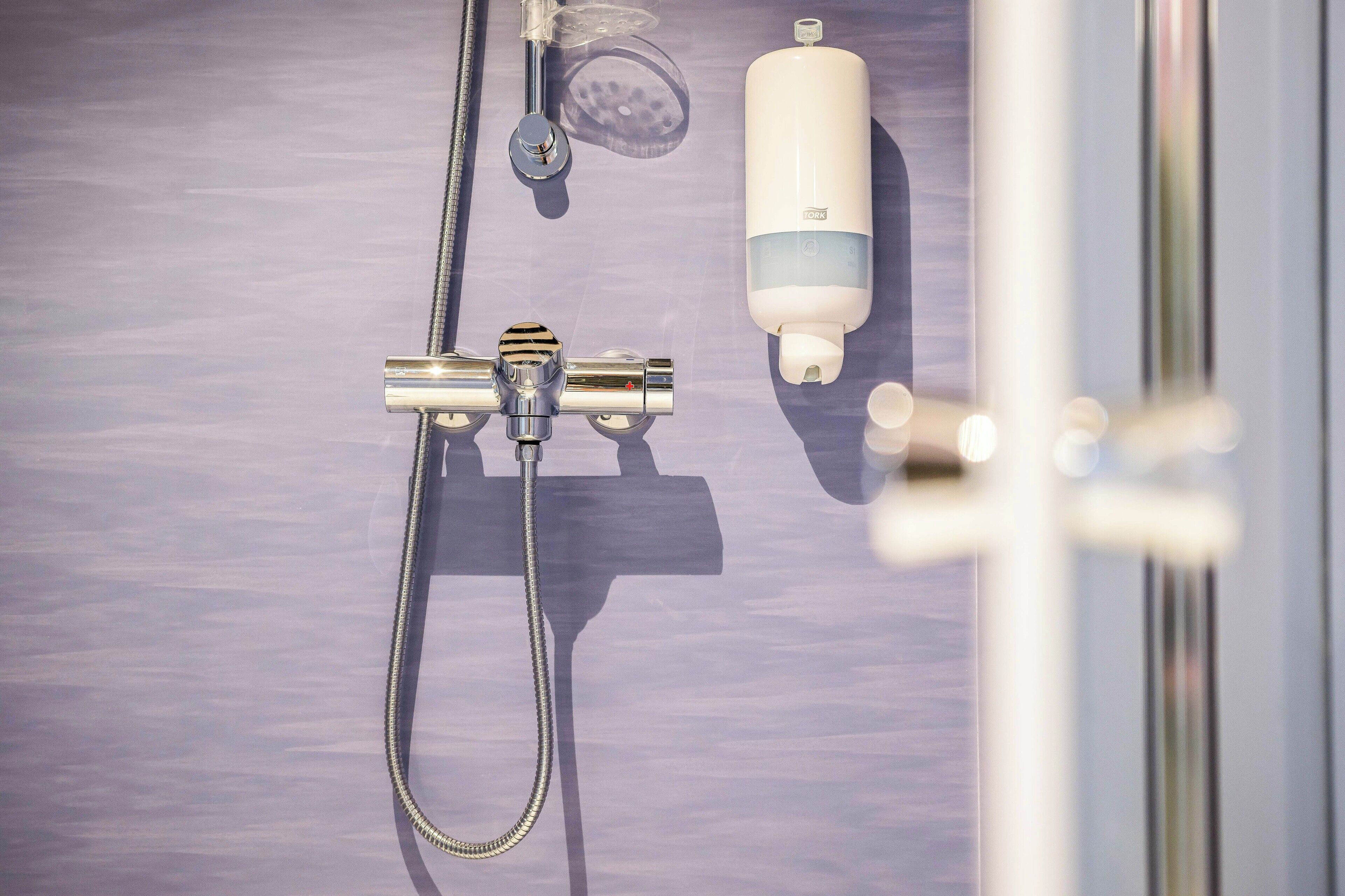 A shower area with a handheld showerhead, a handheld shower attachment, and a soap dispenser.