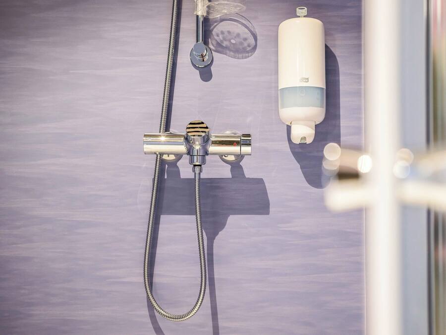 A shower area with a handheld showerhead, a handheld shower attachment, and a soap dispenser.