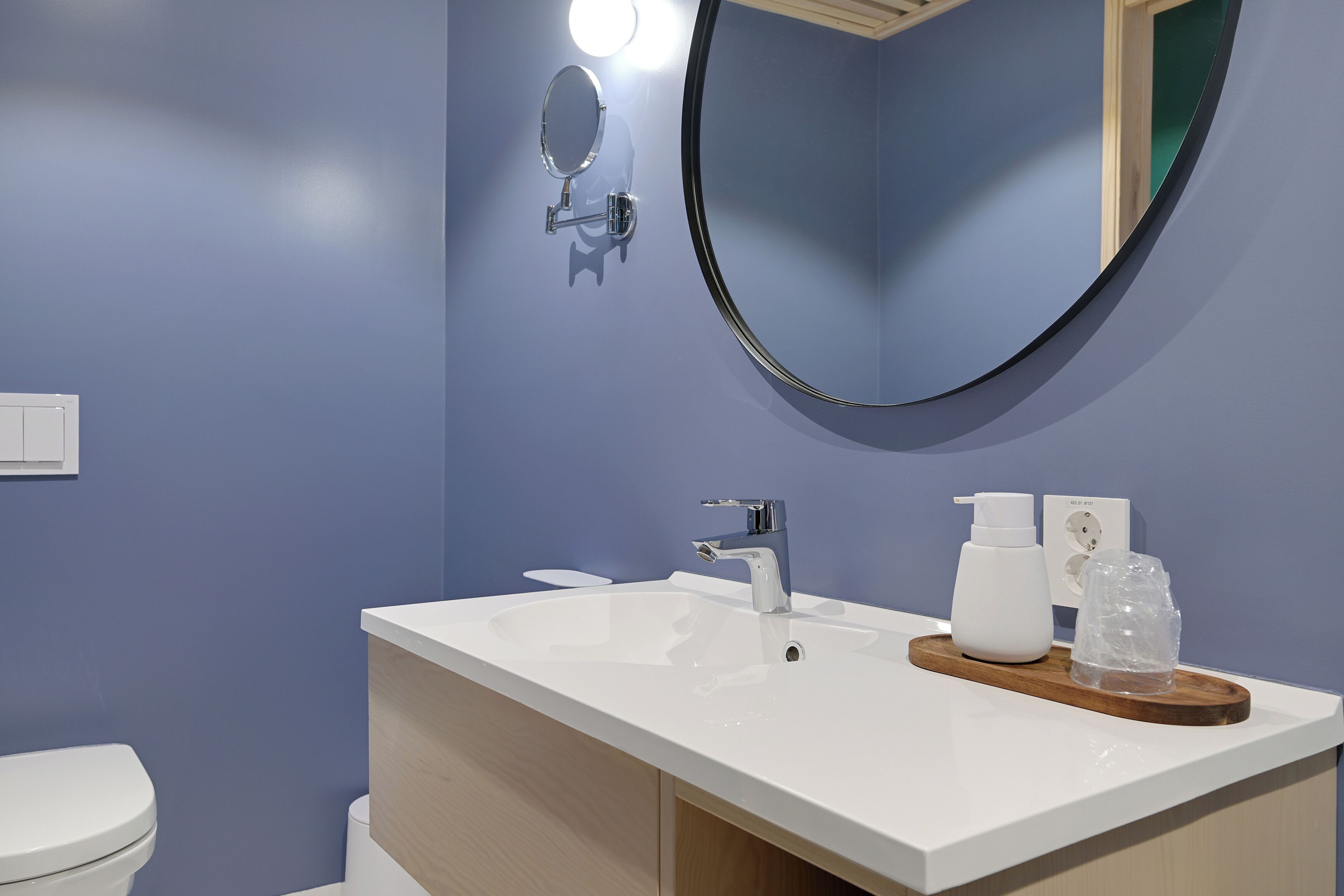 A bathroom with a white sink, a mirror, a toilet, and a wooden tray with toiletries.