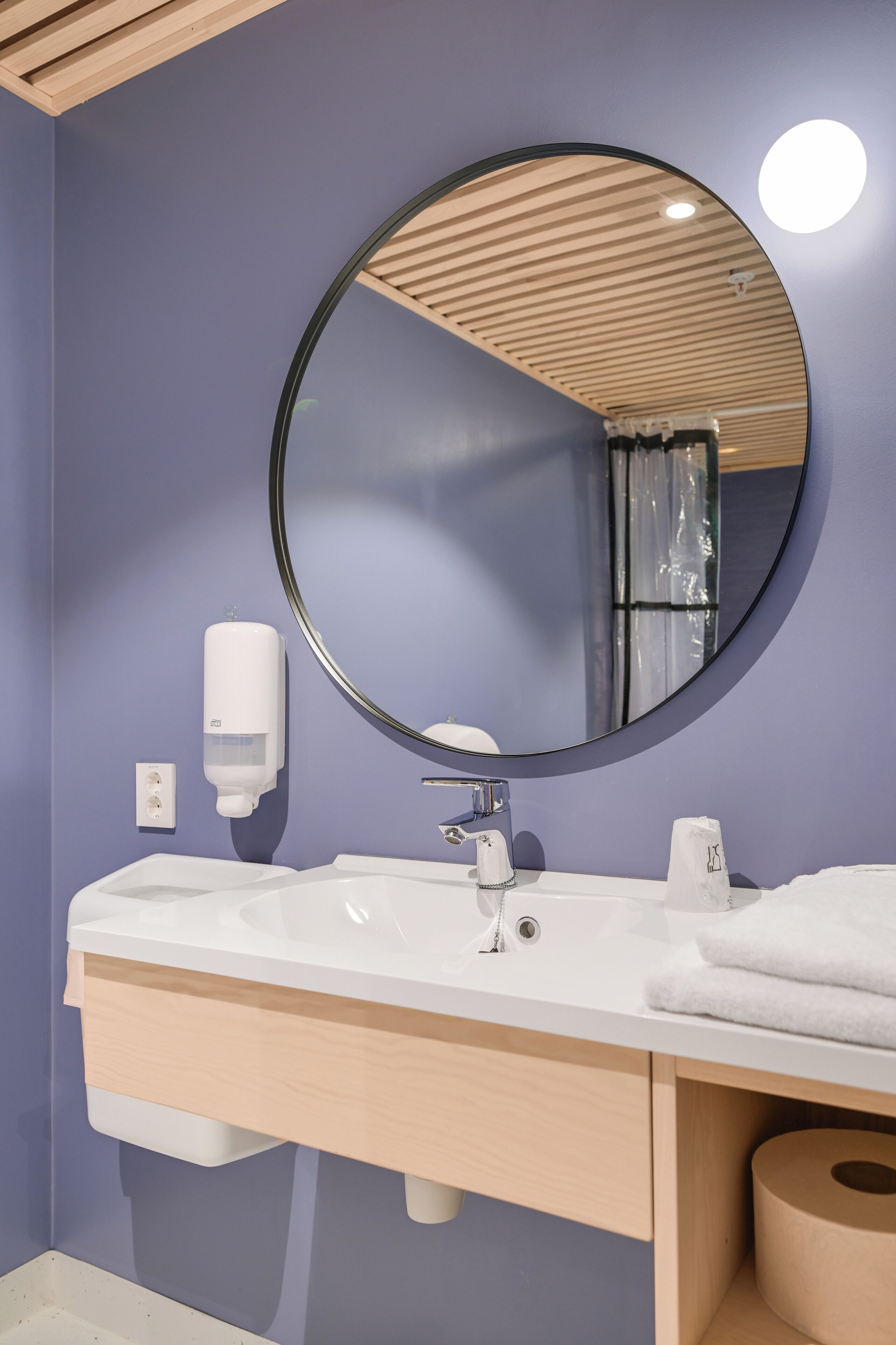 A bathroom with a round mirror, white sink, and wooden vanity.