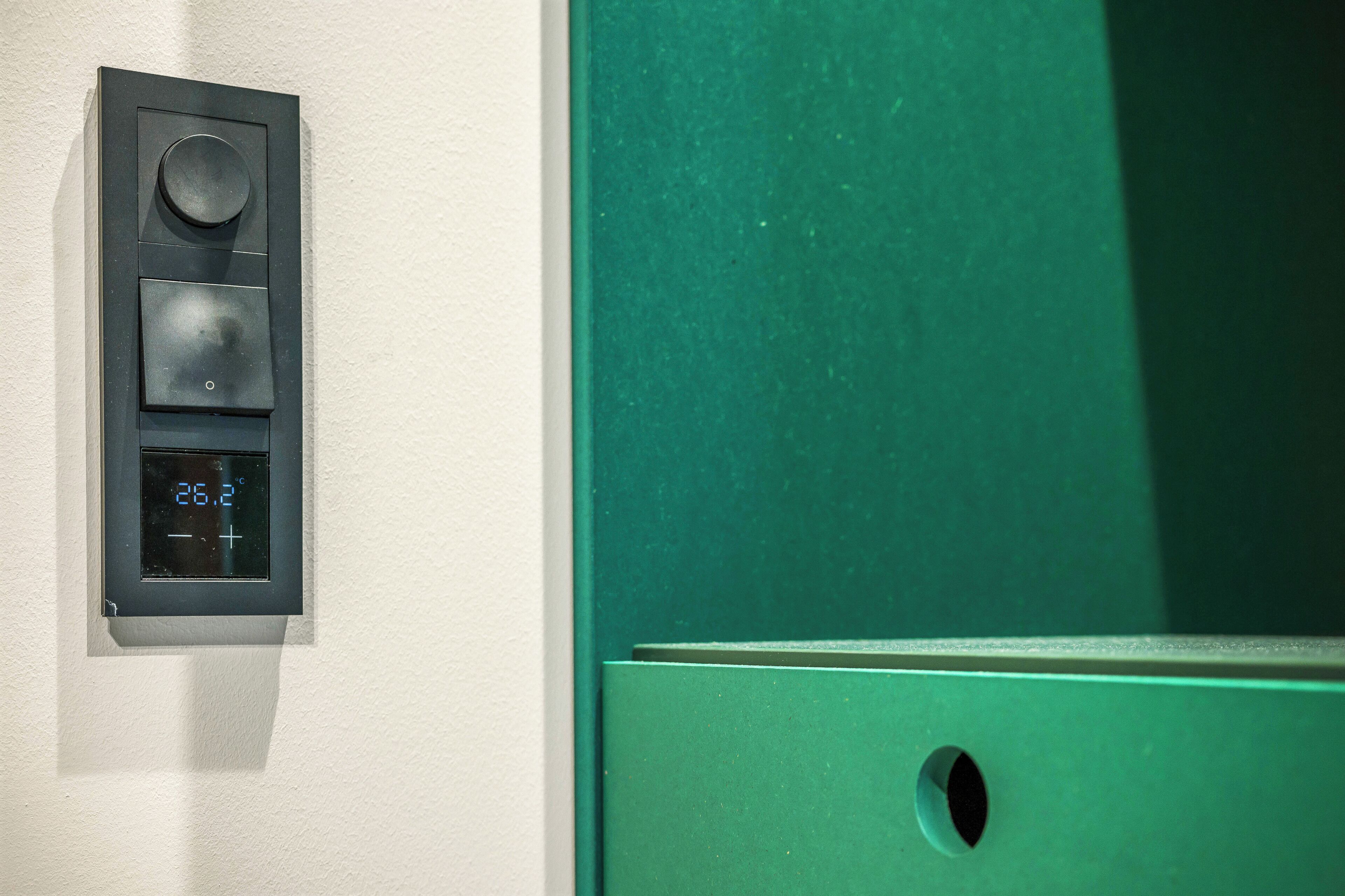 A thermostat with a digital display, a round knob, and a square button on a wall.