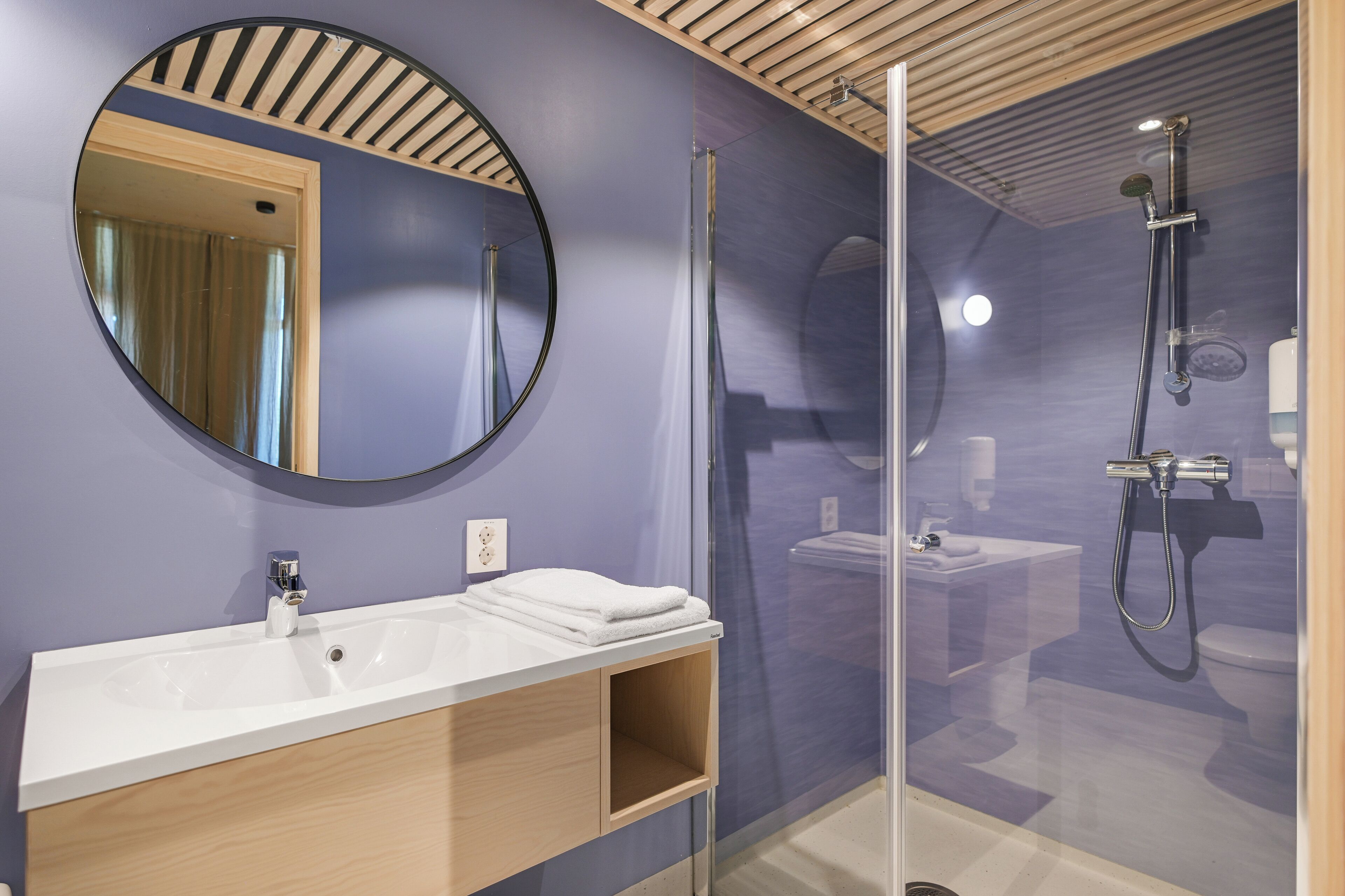 A modern bathroom with a round mirror, a white sink, and a glass-enclosed shower area.