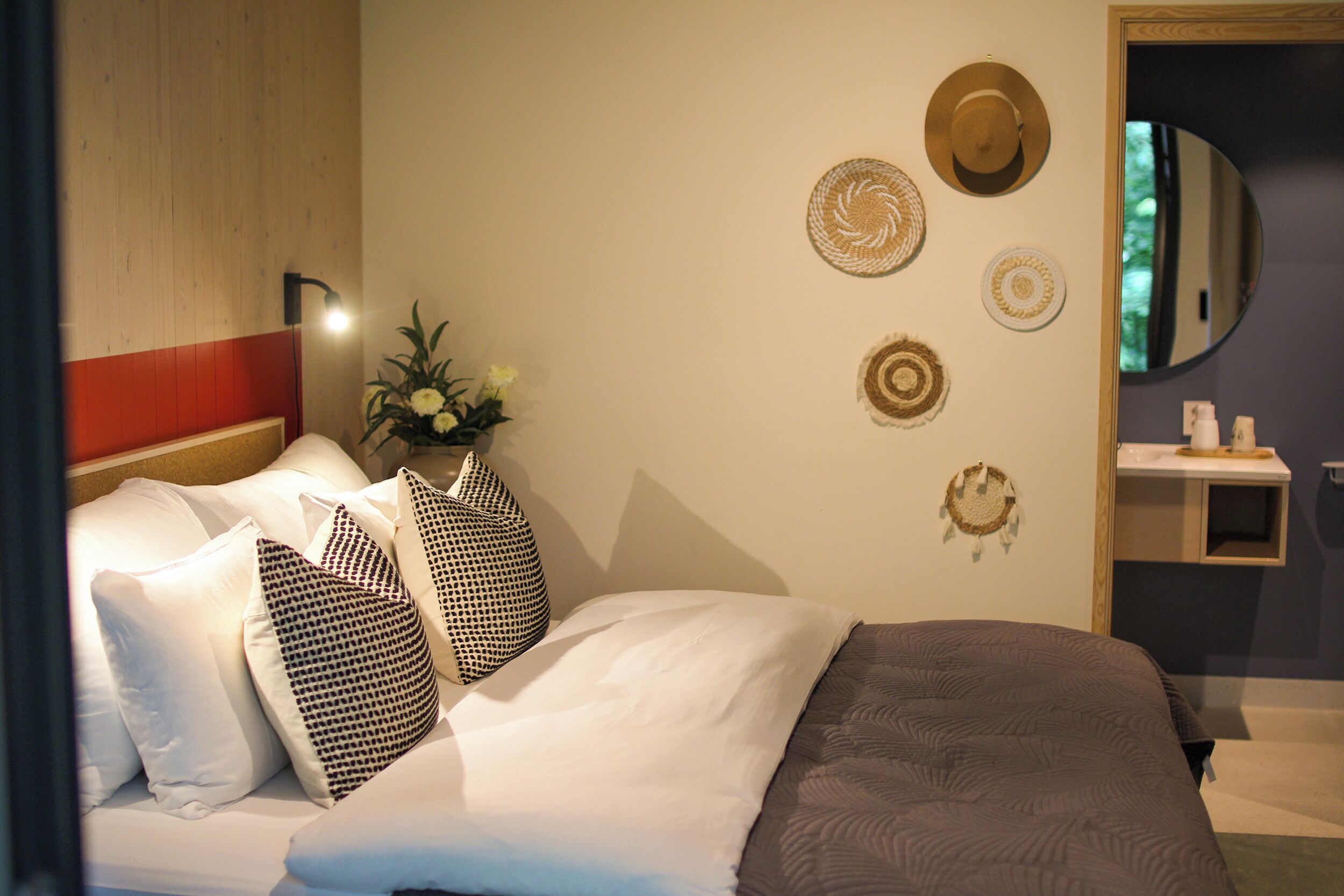 A hotel room with a bed, pillows, wall decor, a mirror, and a small shelf with toiletries.