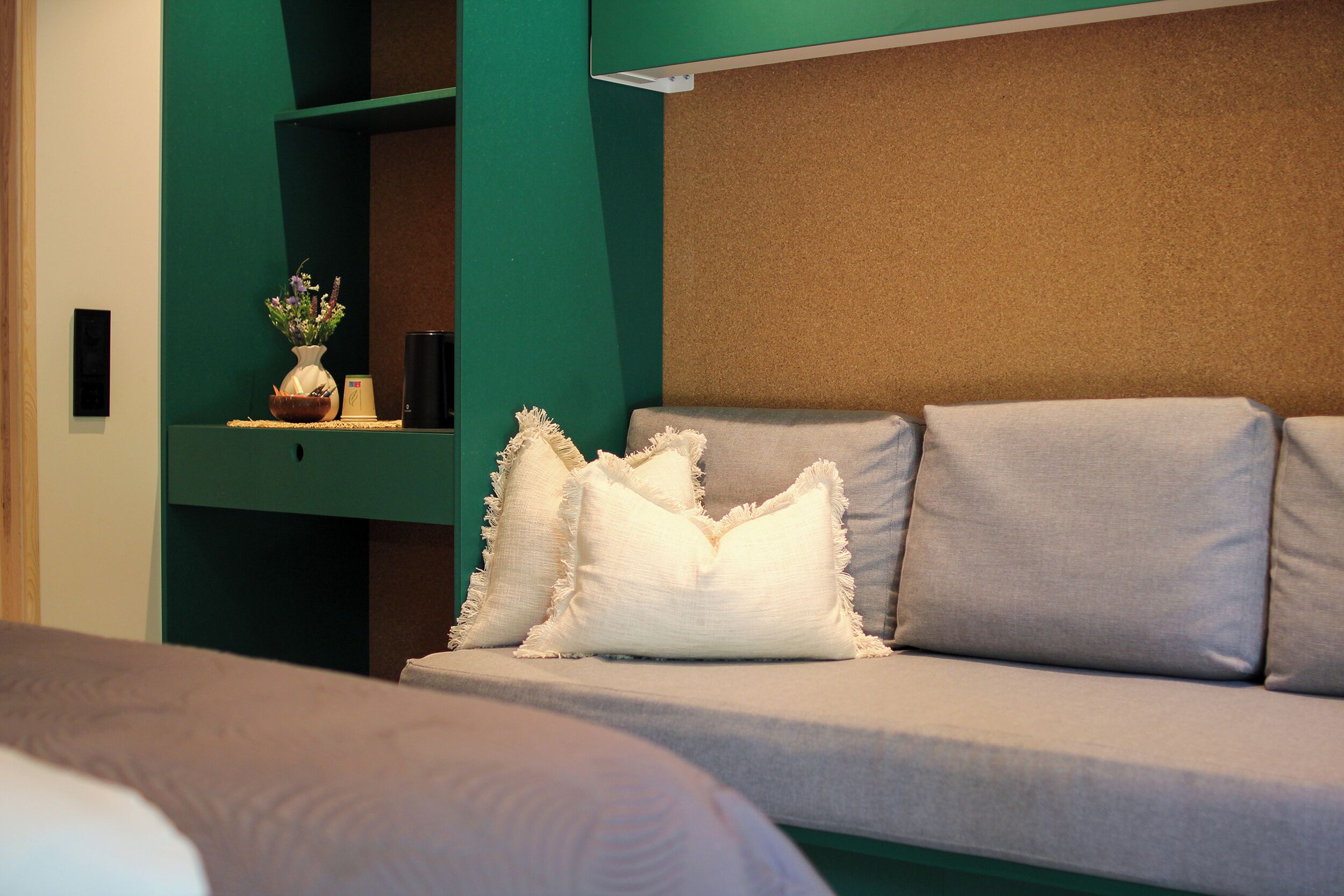 Een moderne hotelkamer met een bank, decoratieve kussens, een vaas met bloemen en een groene accentmuur.